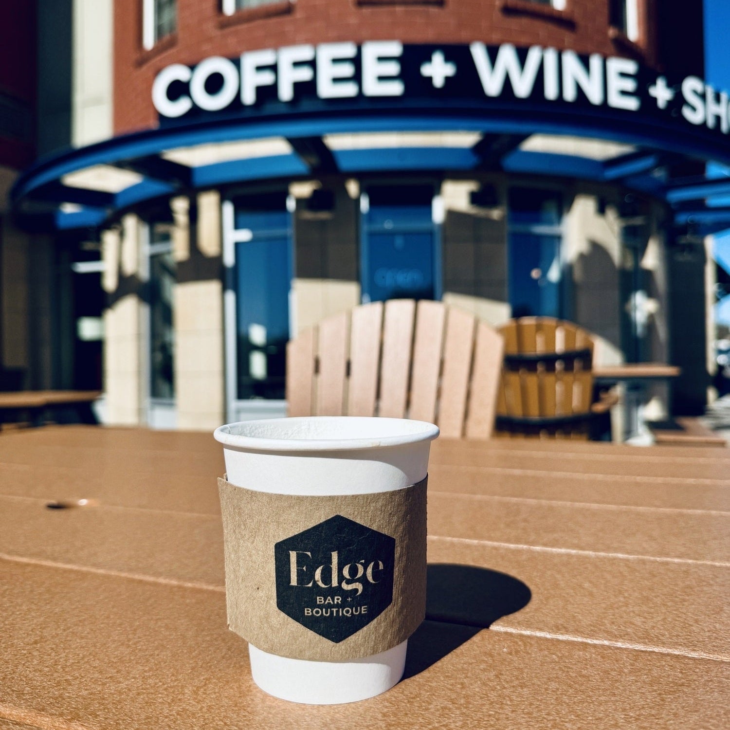 Coffee cup with 'Edge' branding in front of a coffee and wine shop.