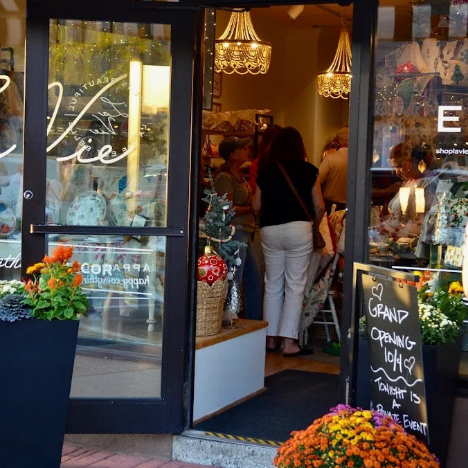 Storefront with striped awning, potted plants, and people entering.